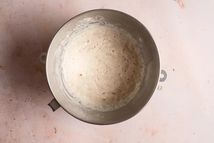 Bước 1: Cho nước ấm đã chuẩn bị vào một cái tô lớn, lần lượt men nở, đường, một cốc bột mì đa dụng vào trộn đều và đợi bột nghỉ 30 phút.