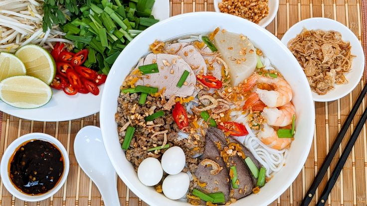 Bước 3: Trình Bày và Thưởng Thức
Trình bày: Cho hủ tiếu vào tô, xếp lên trên tôm, thịt nạc heo, gan, tim, trứng cút, hành phi, tóp mỡ.
Chan nước dùng: Múc nước dùng nóng lên trên, rắc tiêu xay, thêm hành lá, hẹ, cần tàu.
Ăn kèm: Rau sống như giá, xà lách, tần ô, chanh, ớt.