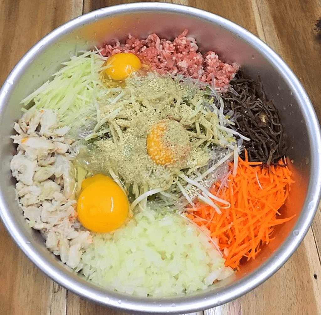 Bước 2: Trộn Nhân Nem
Trong một tô lớn, cho thịt lợn, thịt cua, cà rốt, su hào, miến, mộc nhĩ, nấm hương, giá đỗ vào.
Đập trứng gà vào tô, thêm gia vị: 1 thìa cà phê hạt nêm, 1 thìa cà phê nước mắm, một chút tiêu xay, muối.
Trộn đều hỗn hợp cho đến khi các nguyên liệu hòa quyện vào nhau.
