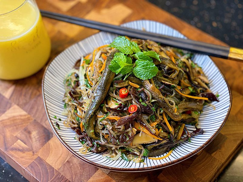 Mẹo Làm Miến Xào Lươn Ngon
Ngâm miến đúng cách: Ngâm miến trong nước lạnh khoảng 10-15 phút trước khi xào, hoặc chần sơ qua nước sôi và để ráo. Điều này giúp miến không bị nhão khi xào.
Phi thơm hành khô: Hành khô được phi vàng tạo hương thơm đặc trưng cho món ăn, nên sử dụng hành khô thay vì hành tươi để tăng thêm độ hấp dẫn.
Xào lươn với lửa lớn: Khi xào lươn, nên dùng lửa lớn để thịt lươn săn lại, giữ độ dai ngon mà không bị bở nát. Xào riêng lươn trước rồi để riêng giúp món ăn có vị đậm đà hơn.
Xào rau với lửa to: Các loại rau như giá đỗ, rau cải nên được xào nhanh với lửa lớn để giữ độ xanh và giòn của rau. Thêm một chút dầu ăn để rau bóng đẹp.
Thêm một ít nước dùng lươn: Để miến không quá khô, bạn có thể thêm một ít nước dùng lươn khi xào miến. Nước dùng sẽ làm miến mềm vừa phải và đậm đà hương vị lươn.
Trộn gia vị đúng lúc: Sau khi xào đều miến với các nguyên liệu, nêm nếm gia vị cho vừa miệng rồi mới tắt bếp. Nhớ trộn đều để sợi miến ngấm gia vị, nhưng tránh xào quá lâu khiến miến mất độ dai.