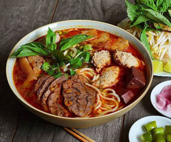 1. Bún bò Huế – Hương vị đậm đà xứ Huế
Bún bò Huế là món ăn nổi tiếng của miền Trung, đặc biệt là thành phố Huế. Nước dùng được nấu từ xương bò và các loại gia vị như sả, ớt, tạo nên hương vị đậm đà, cay nồng đặc trưng. Sợi bún to, dai, ăn kèm với thịt bò tái, giò heo, huyết luộc và rau sống. Món ăn này không chỉ hấp dẫn bởi hương vị mà còn bởi màu sắc bắt mắt và cách trình bày tinh tế.