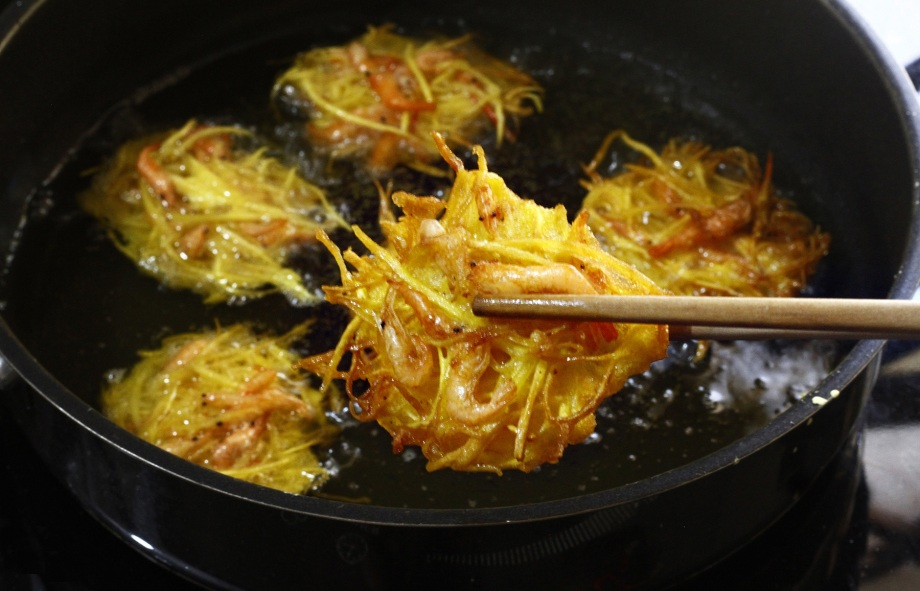 Bước 2: Tạo hình và chiên bánh
Dùng một chiếc muỗng canh hoặc vá nhỏ, múc 1 lượng hỗn hợp khoai môn + tép + bột vừa đủ (khoảng 1 muỗng canh lớn).
Đặt hỗn hợp vào muỗng rồi nhẹ nhàng thả vào chảo dầu nóng. Có thể đặt 1–2 con tép lên trên để bánh nhìn đẹp mắt hơn.
Chiên ở lửa vừa cho tới khi mặt bánh vàng ươm (~2–3 phút), sau đó lật mặt còn lại chiên tiếp cho tới khi vàng đều.
Vớt bánh ra và đặt lên giấy thấm dầu để “giảm béo” và giữ vỏ bánh giòn hơn.
Lặp lại cho tới khi hết hỗn hợp.