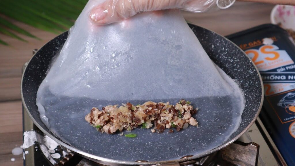 Bước 3: Chuẩn bị khuôn và cách tráng bánh

Sau khi bột đã nghỉ, bạn tiến hành phần tráng bánh.

Quét một lớp dầu mỏng lên khuôn tráng bánh (hoặc chảo) để khi tráng bánh sẽ dễ gỡ. Đun nước sôi trong nồi hấp ( đun ở lửa vừa).

Múc khoảng 2–3 thìa bột cho vào khuôn, xoay nhẹ để bột lan đều một lớp mỏng — mục tiêu là lớp bánh thật mỏng (khoảng 1–2 mm nếu có kinh nghiệm).

Đậy vung, hấp trong khoảng 1–2 phút (tuỳ độ dày và khuôn), tới khi mặt bánh từ đục chuyển trong và không còn ươn ướt.

Cho phần nhân đã được xào từ trước, bỏ dọc theo chiều bánh và đặt ở giữa bánh, đậy nắp một chút cho phần nhân được nóng.

Dùng một chiếc que gỗ hoặc phới nhỏ nhẹ nhàng cuốn gấp 2 chiều về phần nhân sau đó lấy blánh ra khỏi khuôn, đặt lên dĩa.

Lần lượt thực hiện cho tới hết hỗn hợp bột. Khi đặt bánh lên dĩa, bạn có thể xếp chồng nhẹ và che bằng khăn sạch để bánh không bị khô.

Lưu ý: nếu bạn thấy bánh tráng xong bị rách, có thể do lớp bột dày hoặc khuôn chưa được dầu mỏng đều. Ngược lại, nếu bánh quá mềm và khó trượt khỏi khuôn, có thể do hấp chưa đủ hoặc lượng dầu quá ít.